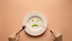 A person prepares to eat from a plate with a sad face, representing the emotional impact of eating disorders.